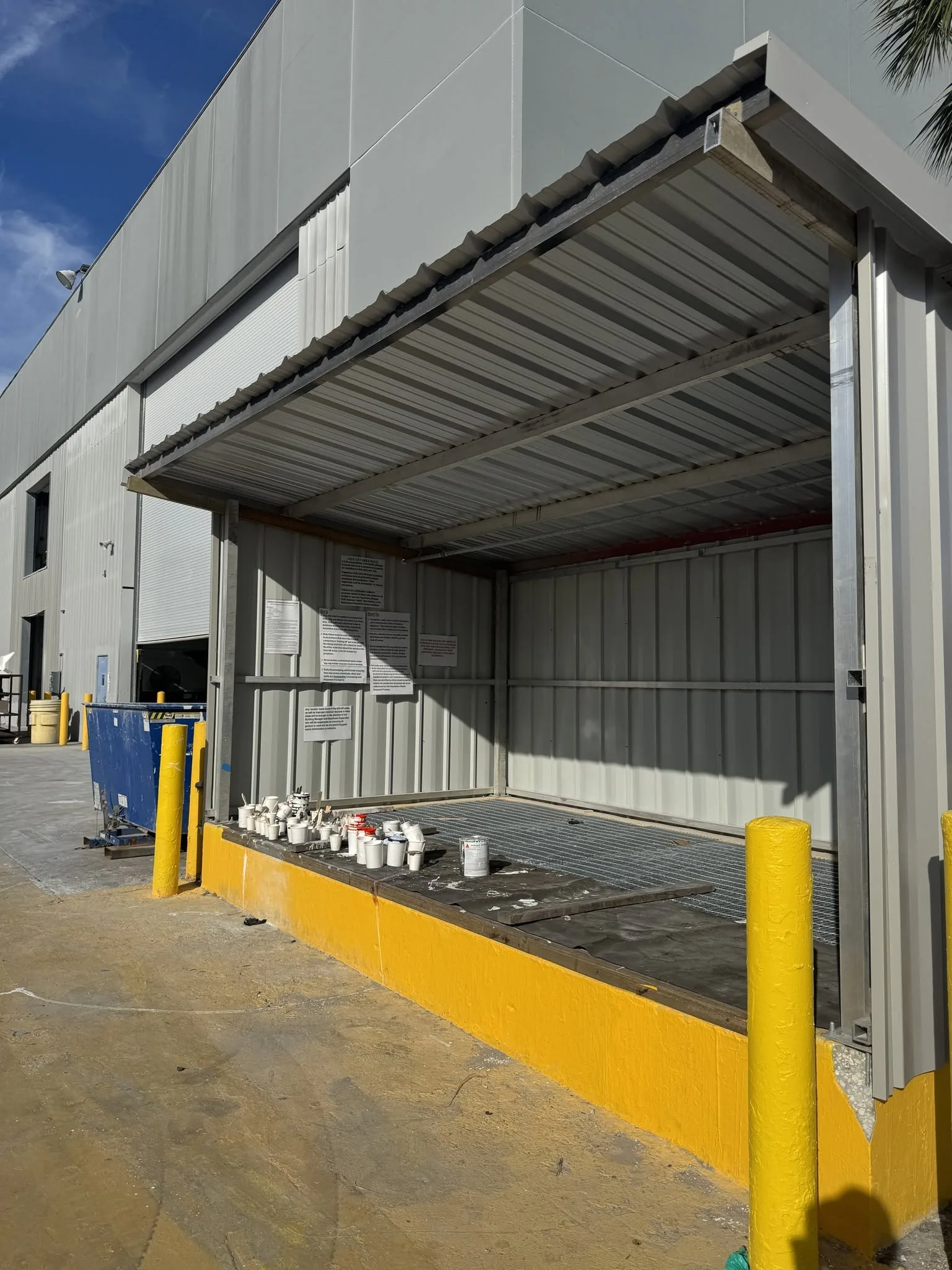 Commercial steel building exterior with roll-up door and safety bollards.